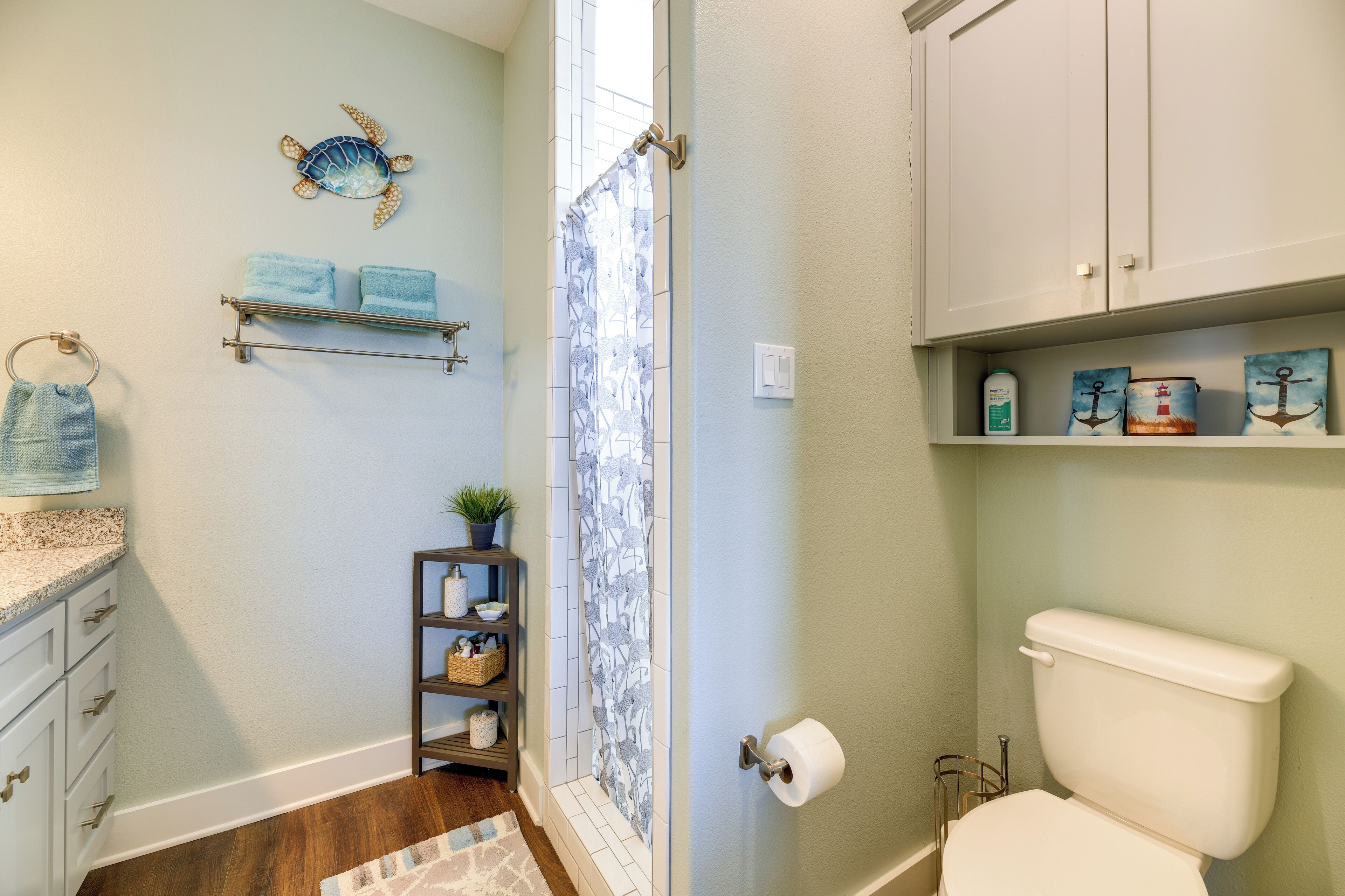 Une salle de bain équipée de toilettes, d’un rideau de douche, d’un porte-serviettes et d’une étagère où sont disposés des objets décoratifs.