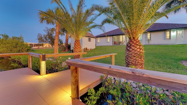 A wooden deck with a stone wall and a small pond, surrounded by palm trees and a grassy lawn. - Waterfront Port Charlotte Vacation Rental w/ Dock! (Port Charlotte)