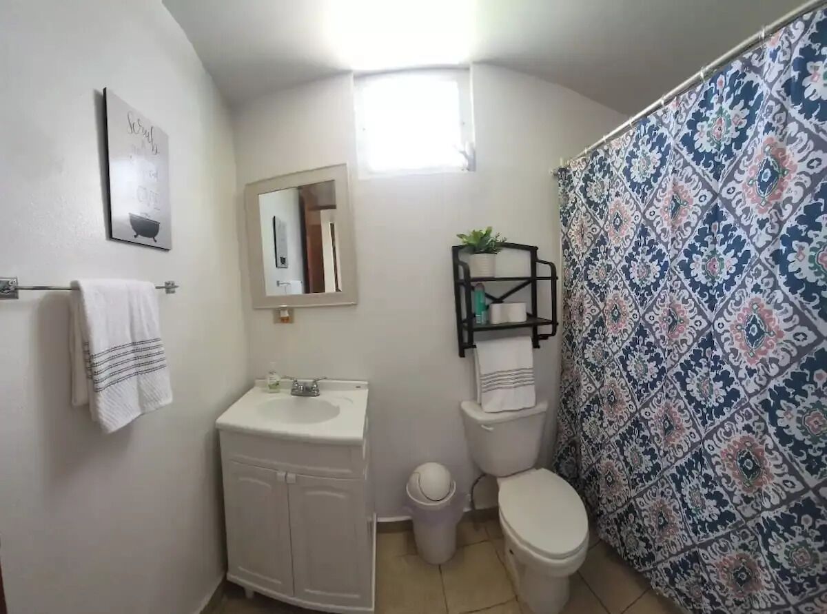 Un baño con lavamanos blanco, inodoro y cortina de ducha estampada.