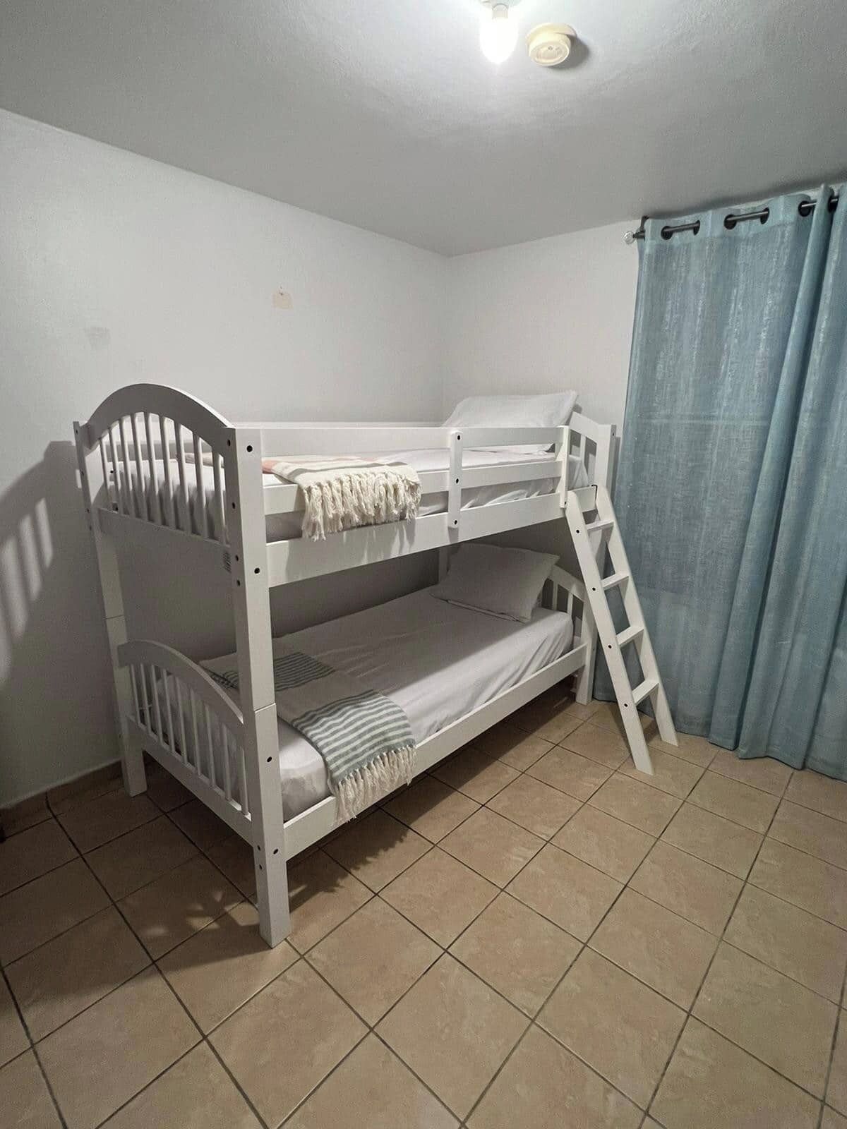 A bunk bed room with a ladder, white walls, and a blue curtain.