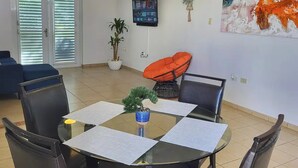 Un comedor con mesa de vidrio, sillas negras, una planta azul en maceta y un cuadro en la pared.