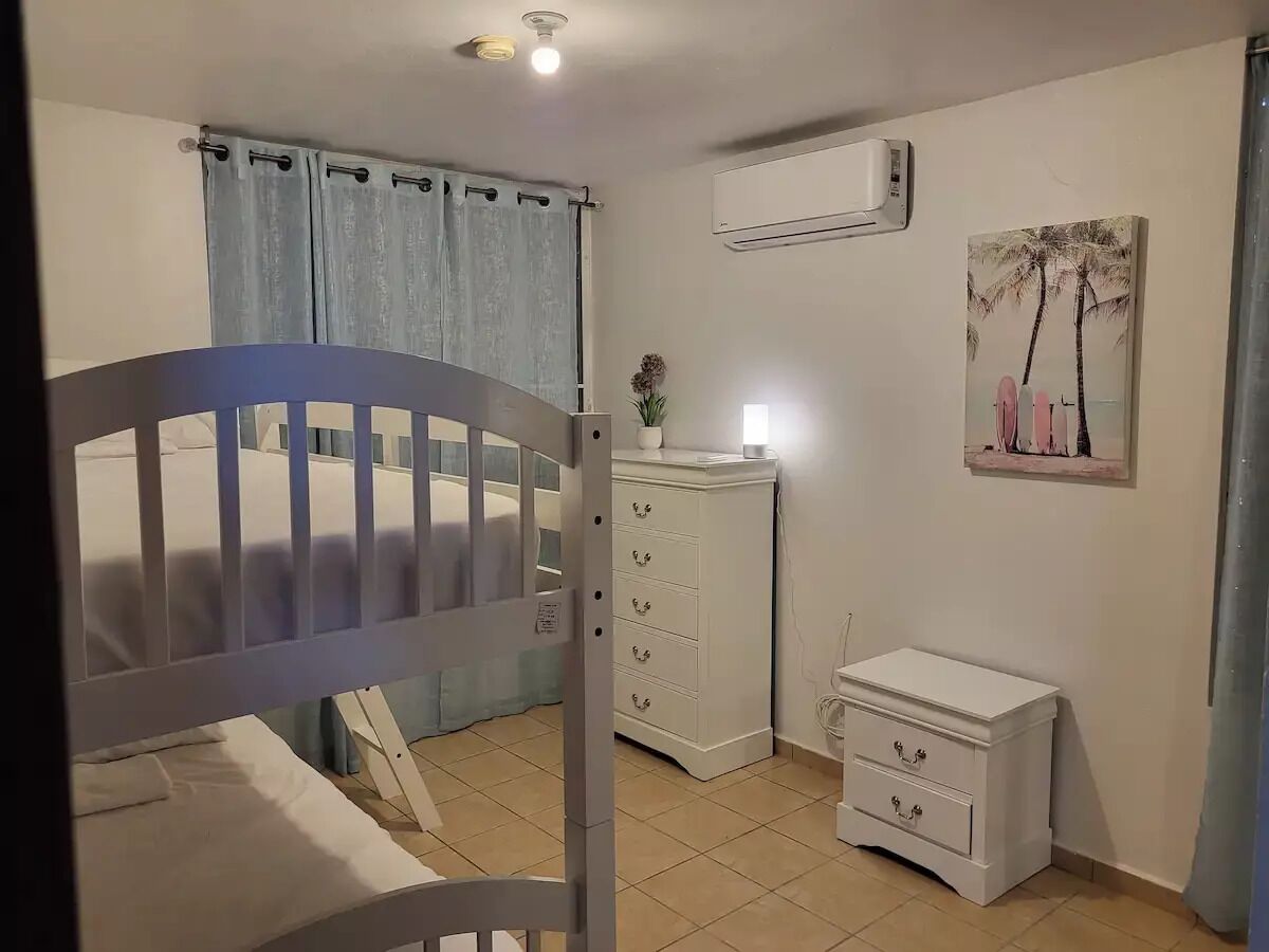 A bedroom with a bed, a dresser, a nightstand, an air conditioning unit, and a wall-mounted picture.
