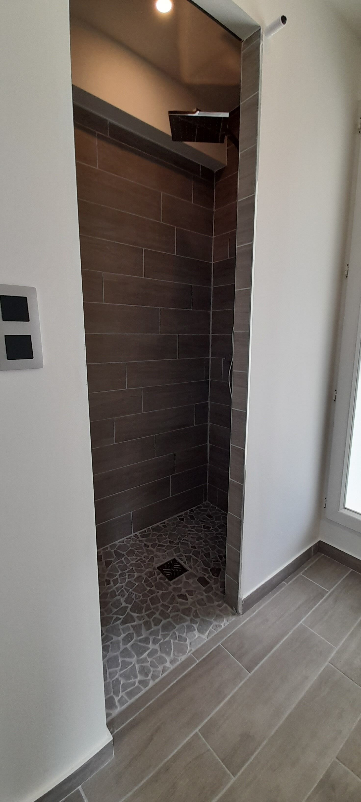 A modern bathroom with a shower area featuring dark brown tiles and a stone-patterned floor.
