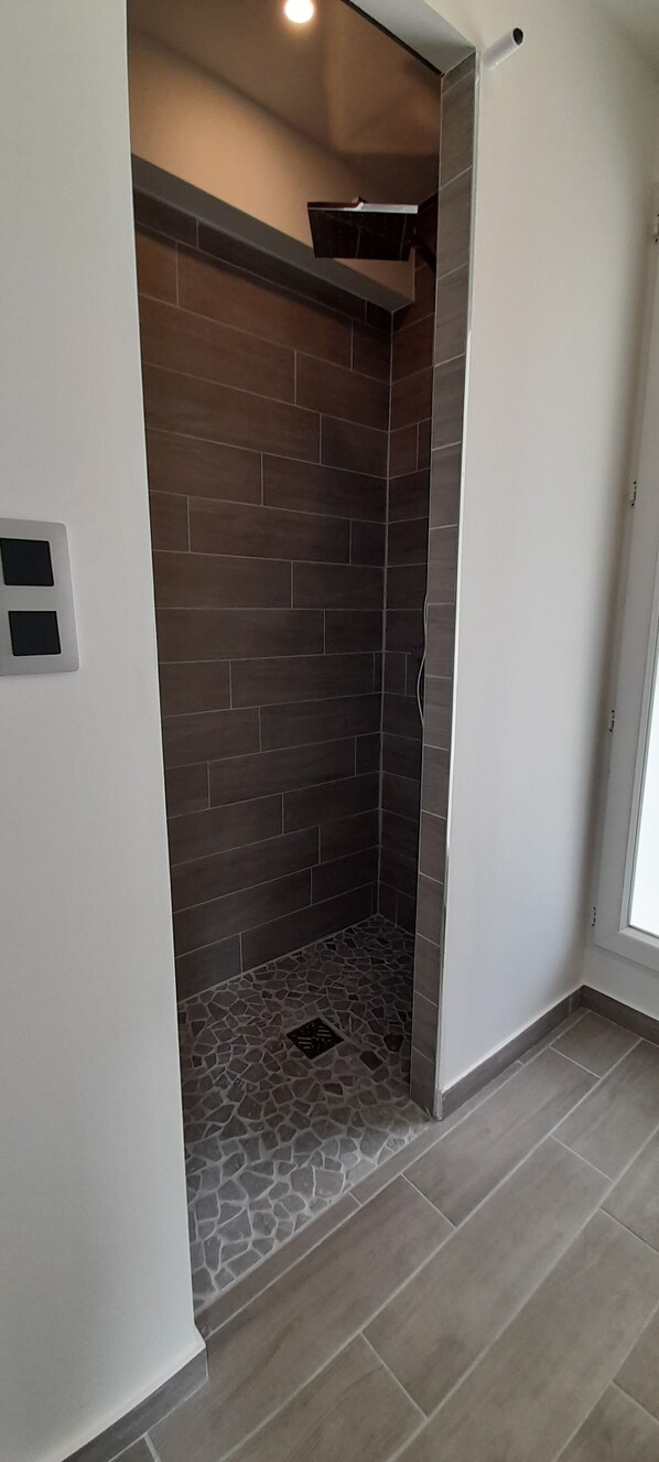 A modern bathroom with a shower area featuring dark brown tiles and a stone-patterned floor. - Sur les pas de Pagnol (Aubagne)