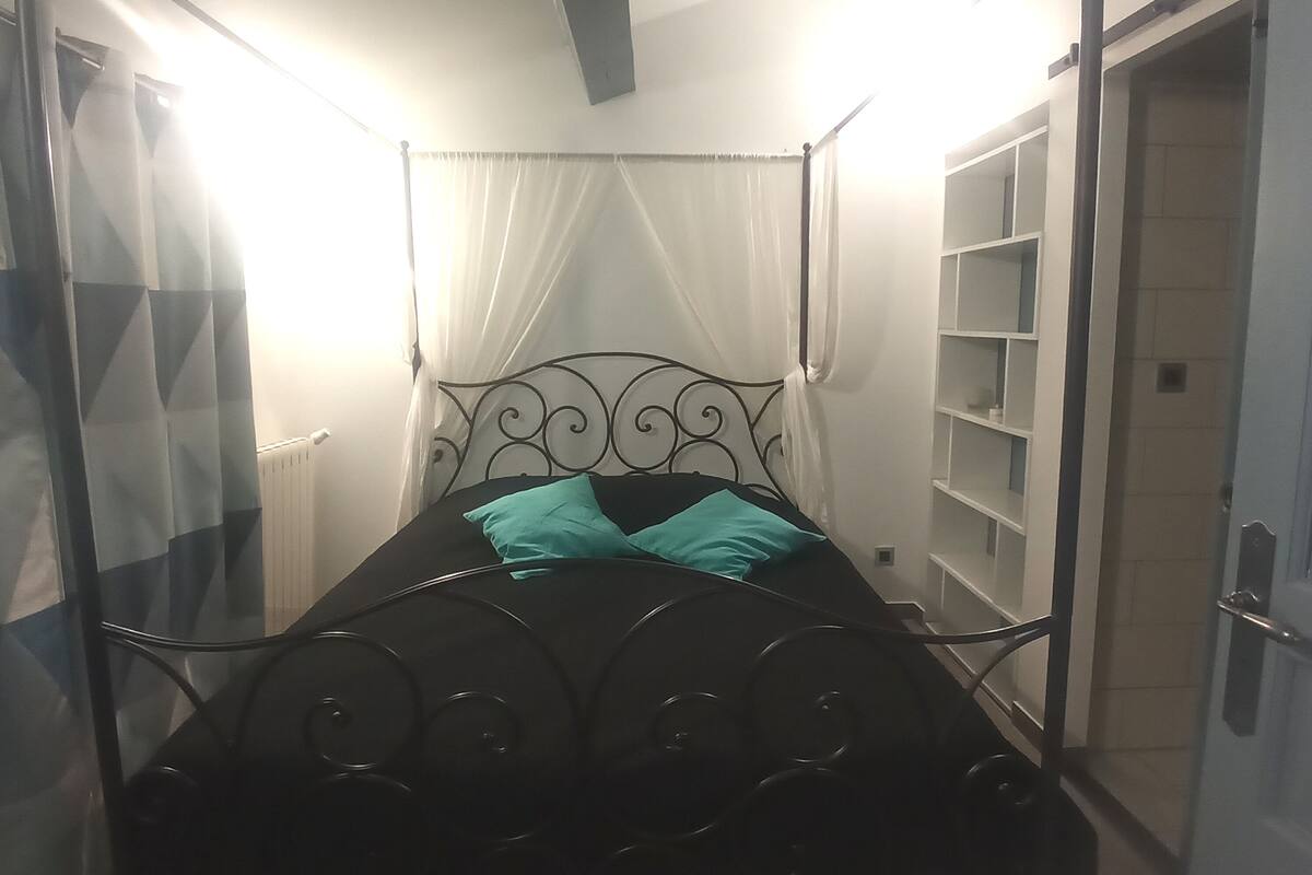 Una cama con estructura metálica, dosel y un par de almohadas color turquesa.