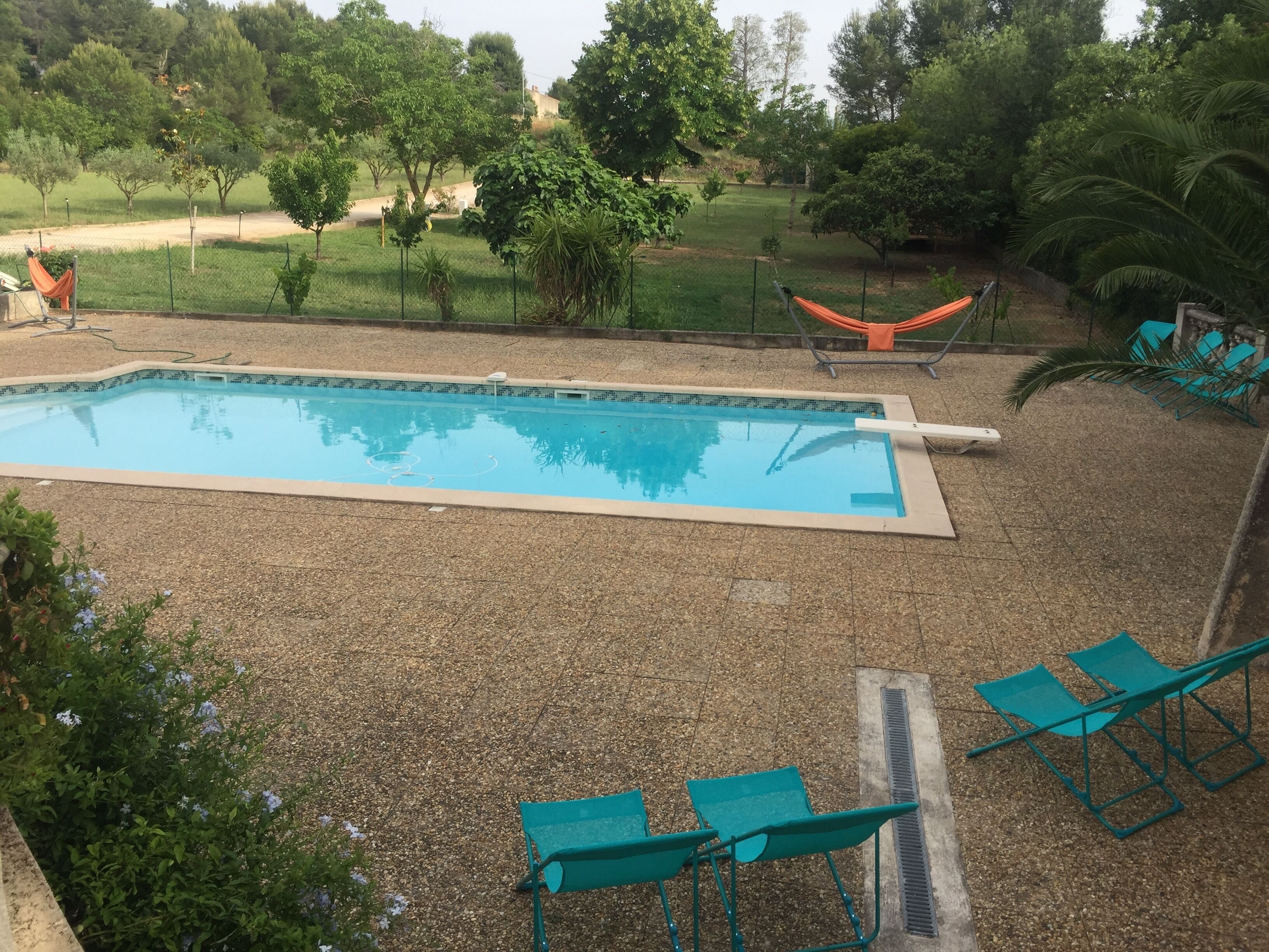 Una piscina rettangolare con bordo piastrellato, circondata da un’area ghiaiosa. Sono presenti poltrone da relax verdi e un’amaca.