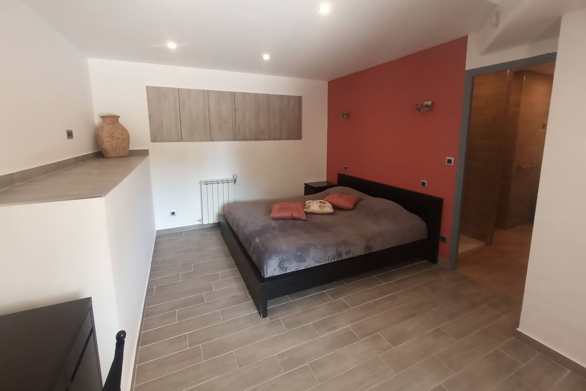 Un dormitorio moderno con cama, radiador, estante en la pared y una pared de acento roja.