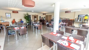 A hotel dining area with multiple tables and chairs, a bar, and a counter with a television.