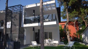 Une maison moderne à deux étages, dotée d’un balcon, d’une terrasse avec mobilier d’extérieur et d’une pelouse bien entretenue.