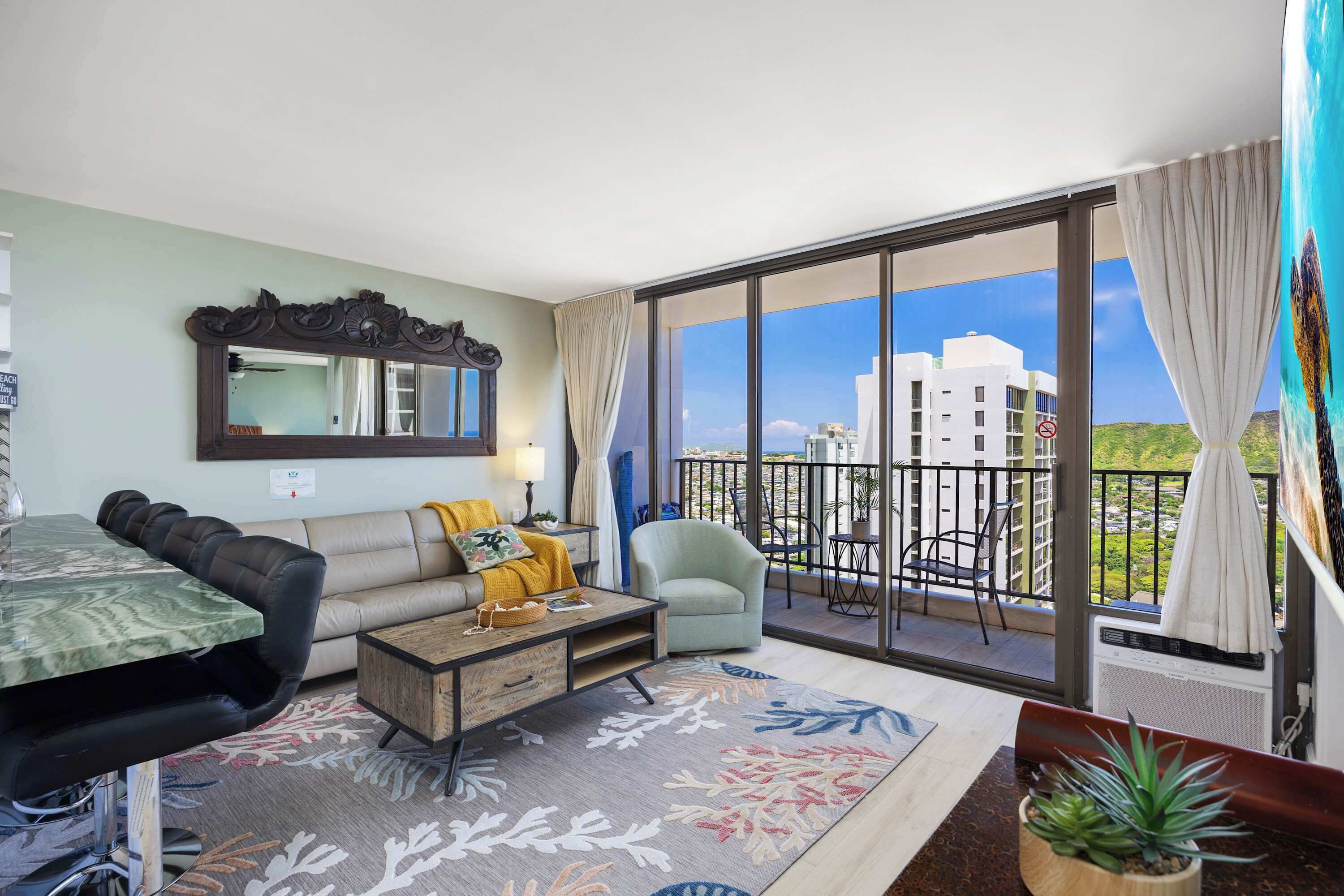 A living room with a sofa, coffee table, and a balcony with a view of buildings.