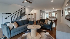 A modern living room with a grey sectional sofa, a round coffee table, and a ceiling fan. - Music City Command Center: 3BR Berry Hill Home (Berry Hill)