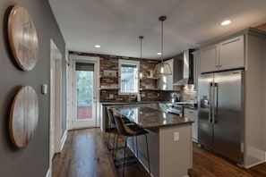 A modern kitchen with a central island, stainless steel appliances, and a brick backsplash. - Music City Command Center: 3BR Berry Hill Home (Berry Hill)