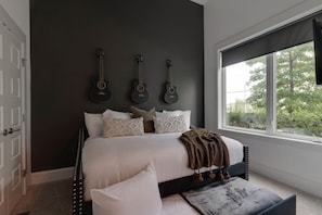 A bedroom with a dark wall, a bed with white bedding, and three guitars mounted on the wall. - Music City Command Center: 3BR Berry Hill Home (Berry Hill)