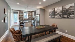 A modern kitchen with a central island, built-in appliances, and a dining area with a dark wood table and leather chairs. - Music City Command Center: 3BR Berry Hill Home (Berry Hill)