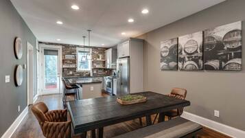 A modern kitchen with a central island, built-in appliances, and a dining area with a dark wood table and leather chairs.