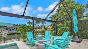 A covered outdoor area with turquoise Adirondack chairs, a round table, and a pool.