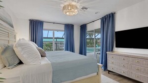 A bedroom with a bed, a television, a dresser, and large windows.