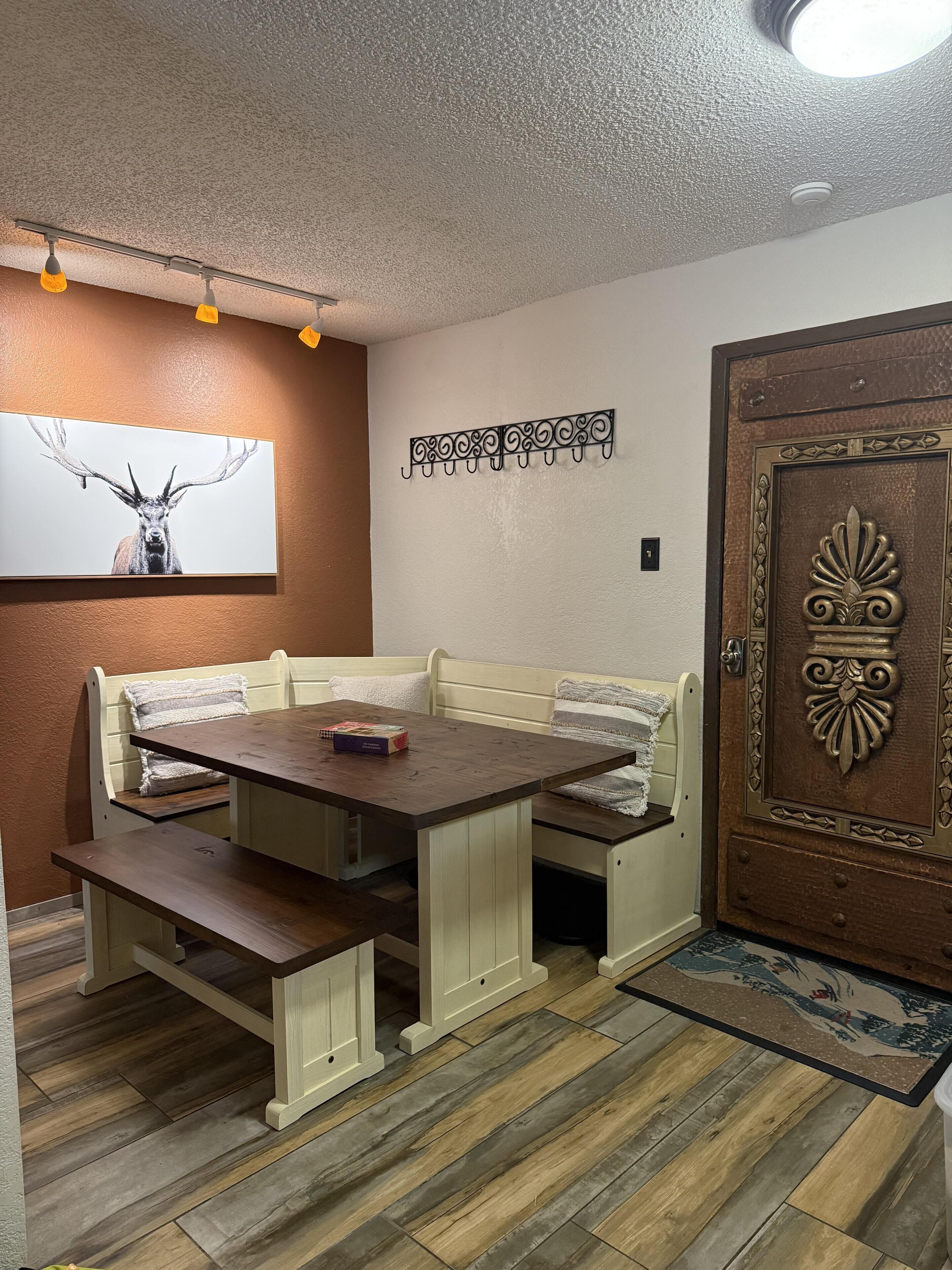 A cozy room with a wooden table, bench seating, a decorative wall piece, and a door with intricate design.
