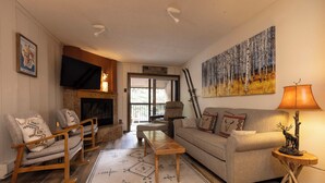 Una sala de estar acogedora con chimenea, un sofá, sillones mecedores y un cuadro en la pared.