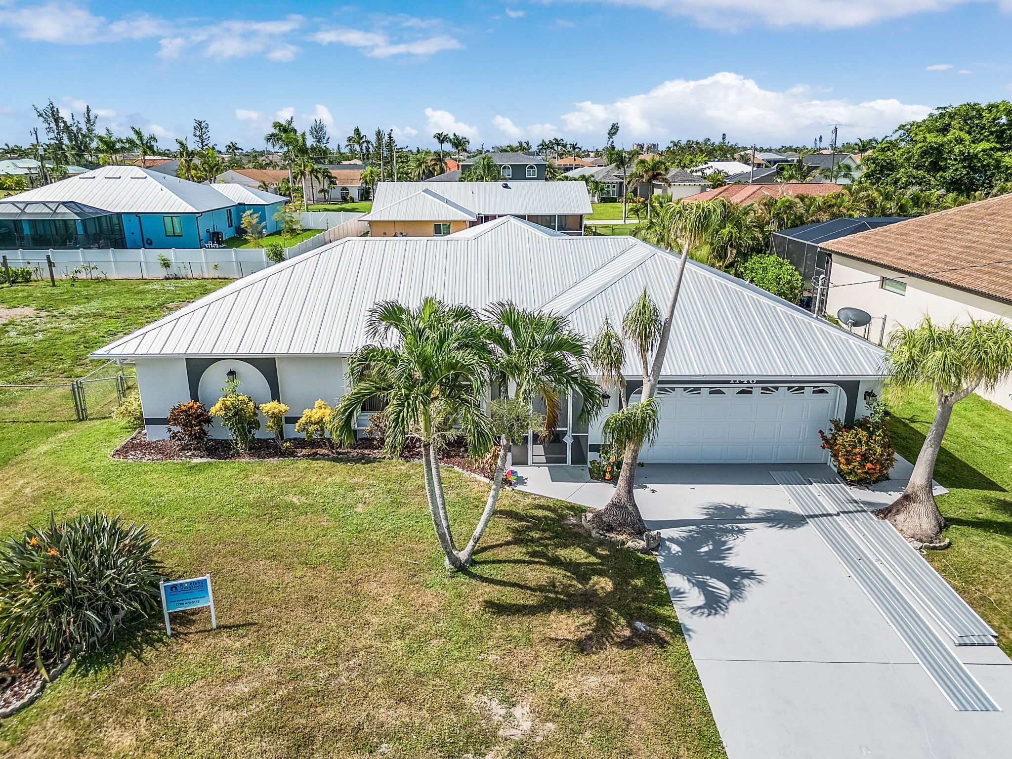 A residential house with a metal roof, a garage, and a well-maintained lawn with palm trees.