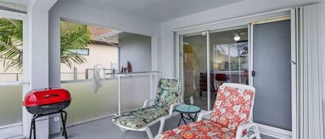 A balcony with a grill, two lounge chairs, and a glass door leading to a patio.