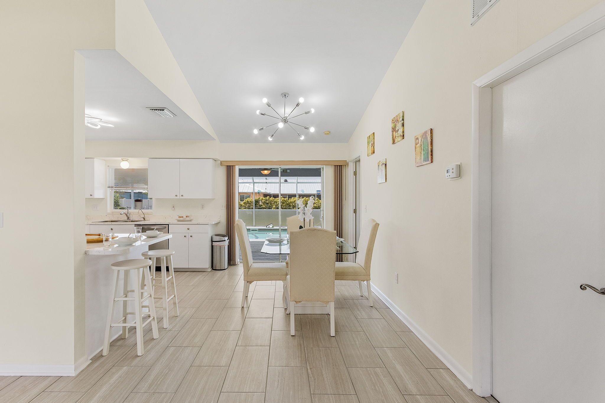 A modern kitchen with a dining area, a view of the outdoors, and a ceiling light fixture.
