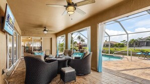 A covered patio area with wicker furniture, a ceiling fan, and a view of a swimming pool. - Pool home on a serene canal, Quiet area for relaxation.- Villa Del Mar - Roelens Vacations (Cape Coral)
