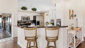 A kitchen with white cabinets, stainless steel appliances, and a central island with two bar stools. - Pool home on a serene canal, Quiet area for relaxation.- Villa Del Mar - Roelens Vacations (Cape Coral)