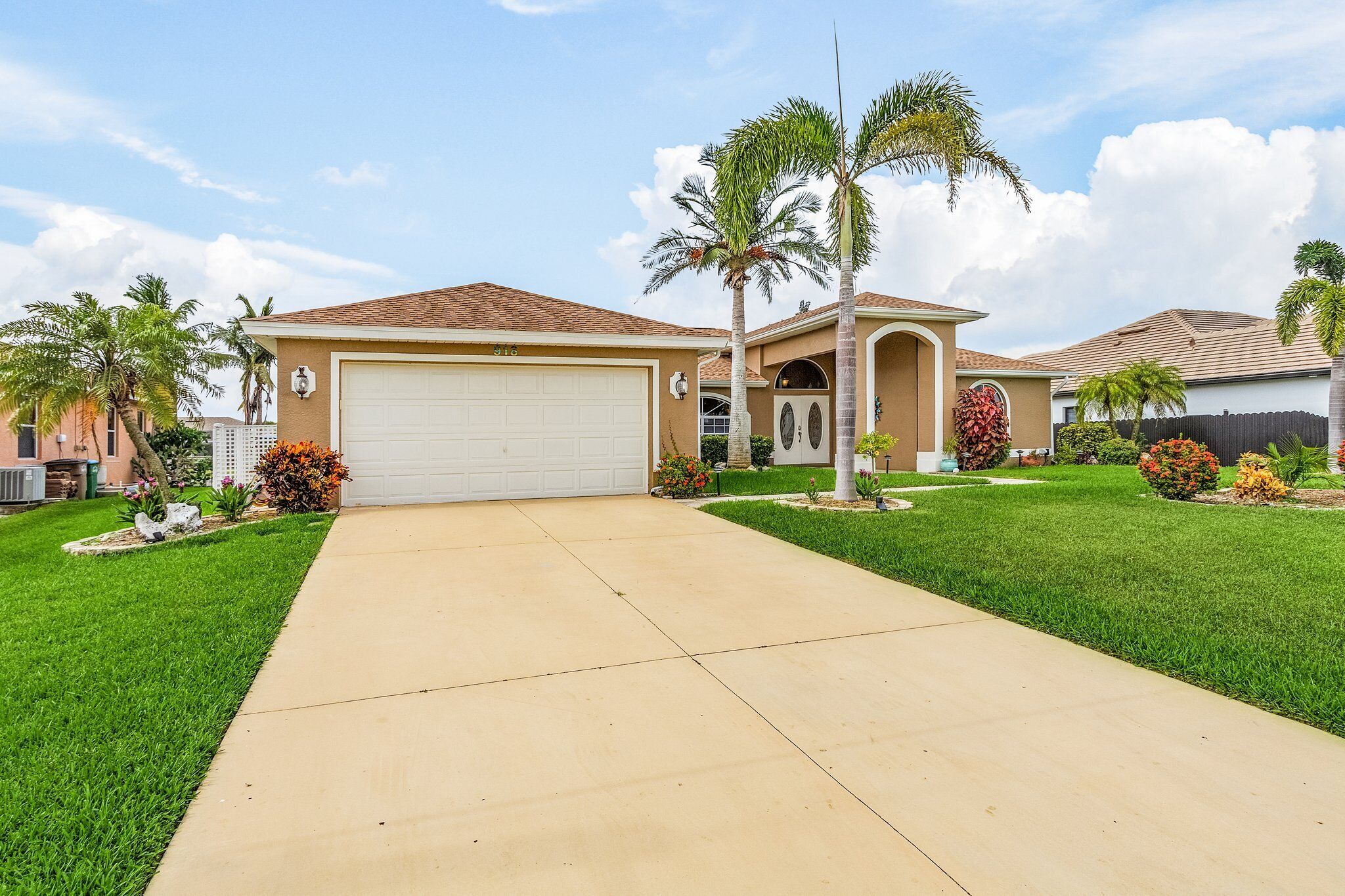 A single-story house with a garage, a well-maintained lawn, and a variety of plants and shrubs.