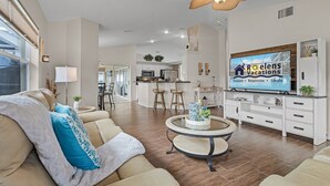 A modern living room with a sofa, coffee table, and TV. There is a kitchen in the background with cabinets and a refrigerator. - Pool home on a serene canal, Quiet area for relaxation.- Villa Del Mar - Roelens Vacations (Cape Coral)