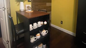 Una cocina compacta con una mesa de madera, un estante con tazas blancas y un florero con flores en la pared.