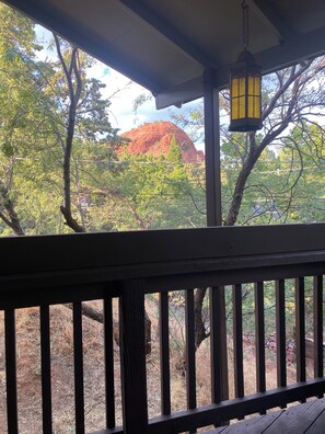 A wooden deck with a view of a red rock formation and trees.