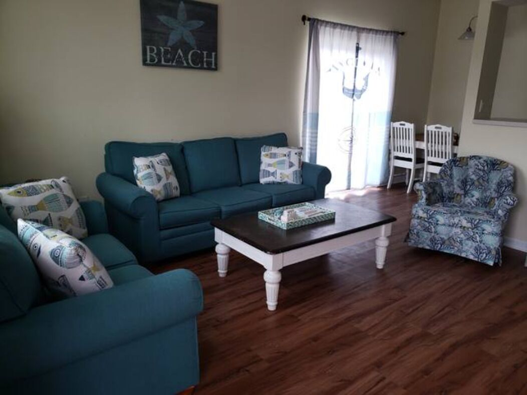 A living room with a teal sofa, a white armchair, and a wooden coffee table.