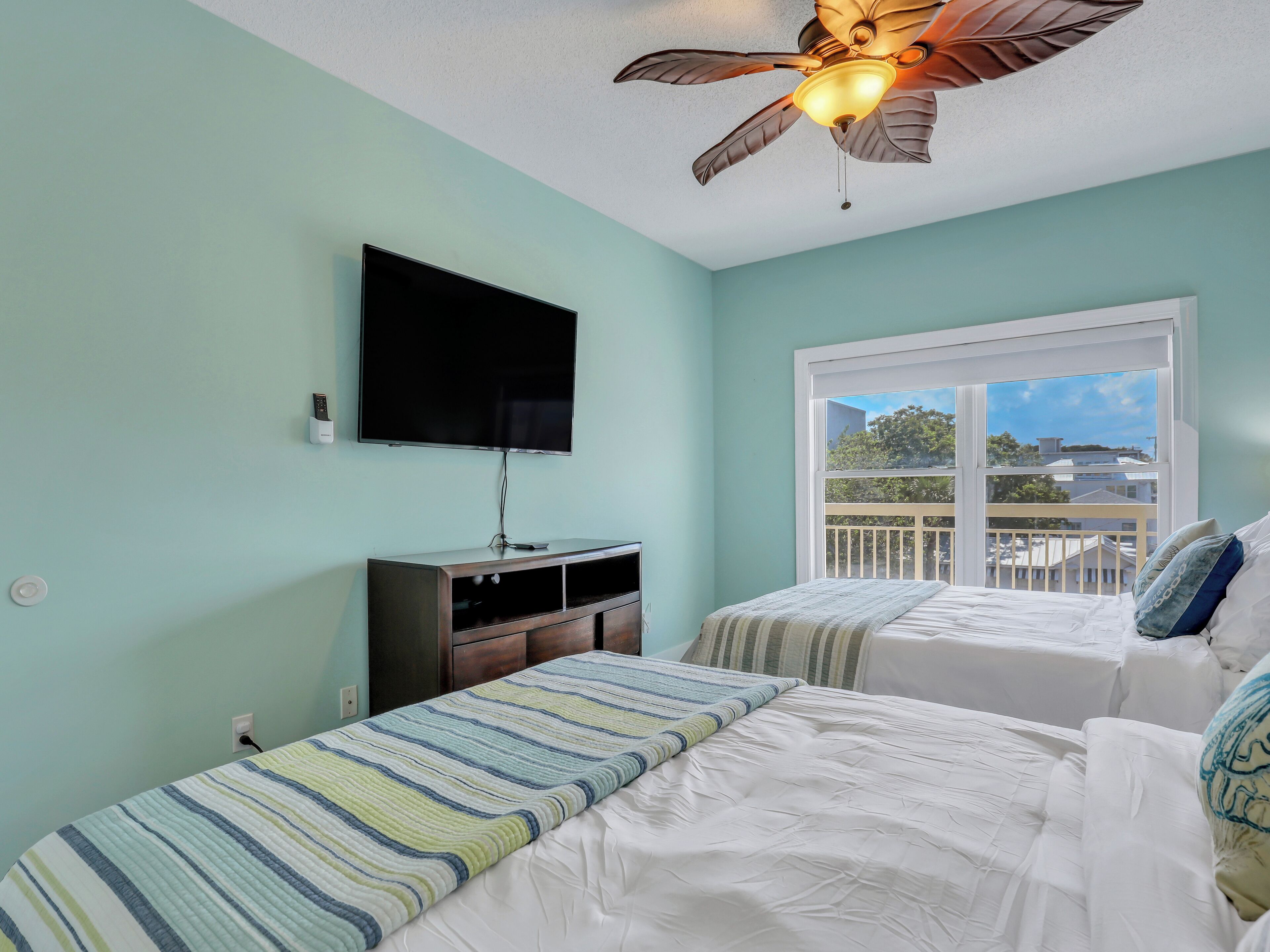 A room with two beds, a ceiling fan, a TV, and a window with a view of the outside.