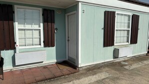 A two-story building with a light green exterior, numbered 2, featuring two windows with brown shutters, a white door, and a small porch area. - Whiskey Bay Lodge #2 (Boothville-Venice)
