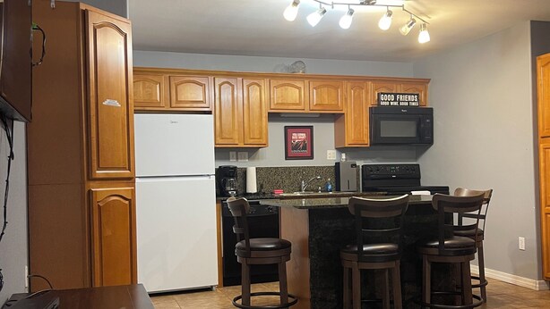 A kitchen with wooden cabinets, a refrigerator, a microwave, and a bar area with stools. - Whiskey Bay Lodge #2 (Boothville-Venice)
