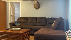 A living room with a brown sectional sofa, a wooden coffee table, a ceiling fan, and a mounted deer head on the wall. - Whiskey Bay Lodge #2 (Boothville-Venice)
