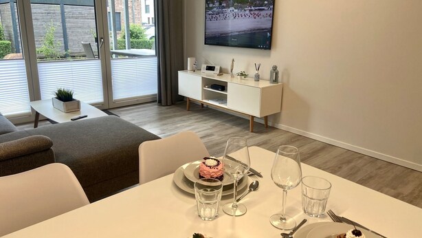 Ein modernes Wohnzimmer mit Essbereich, einem an der Wand befestigten Fernseher und einem Balkon mit Blick auf Gebäude.