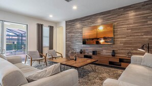 A modern living room with a large flat-screen TV, comfortable seating, a wooden accent wall, and a view through a glass door to an outdoor area. - Waterpark, Arcades, Pool Table, Drive-in Theater, Poker Table: Treasured Days (Davenport)