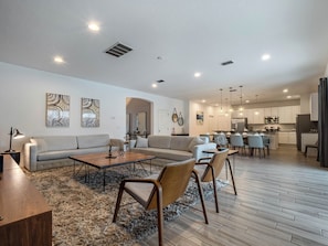 A modern living room with a sofa, coffee table, and chairs. There is a kitchen area with cabinets and appliances visible.