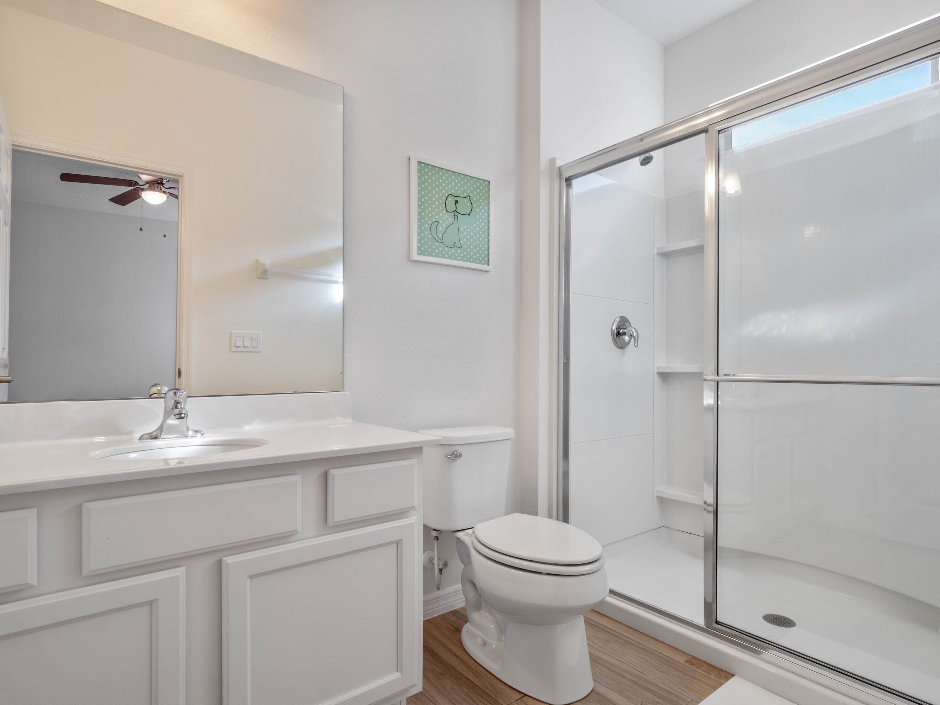 Et moderne badeværelse med et hvidt underskab, toilet og en brusekabine med glasvægge.