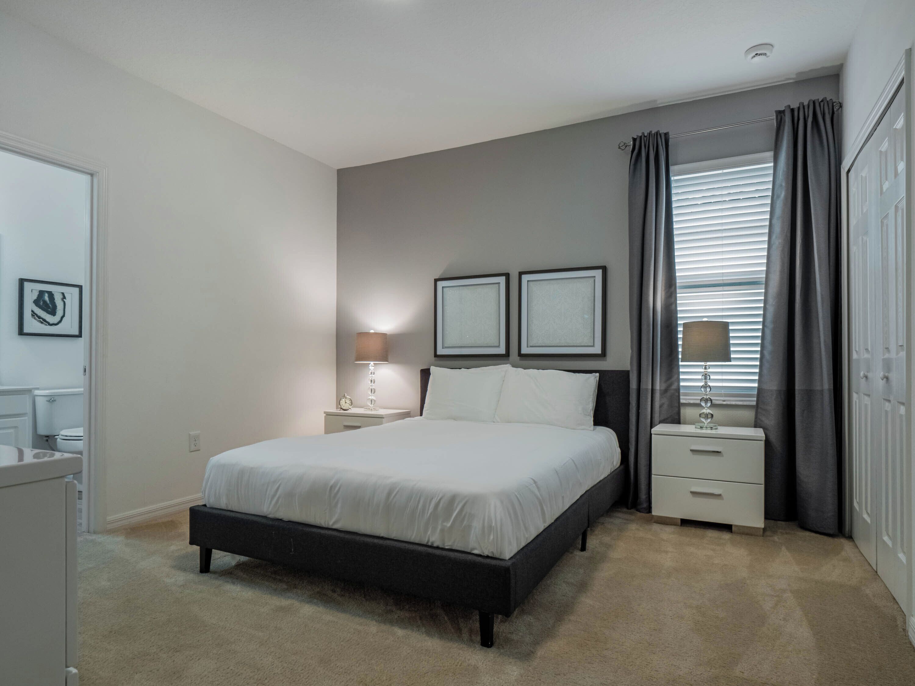 Un dormitorio con cama, mesitas de noche, lámpara y ventana con cortinas.