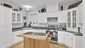 Une cuisine moderne avec des meubles blancs, un îlot central, des appareils en acier inoxydable et des objets décoratifs disposés sur des étagères.
