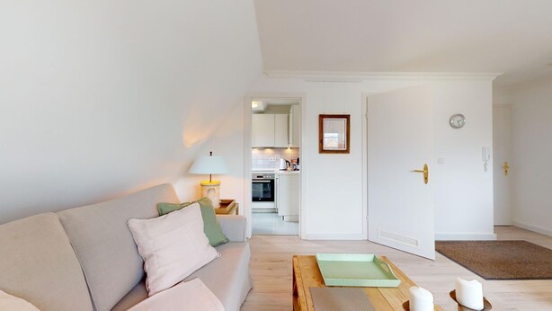 Een moderne woonkamer met een bank, een salontafel en een lamp. Er is een deur naar een keuken.