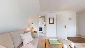 A modern living room with a sofa, a coffee table, and a lamp. There is a door leading to a kitchen area.