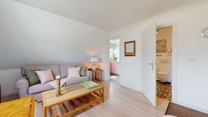 Een woonkamer met een bank, salontafel en lamp. Er is een deur naar een badkamer met toilet en spiegel.
