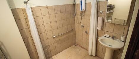 Een kleine badkamer met douche, handgreep en wastafel.