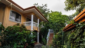 A house with a covered porch, a brick pathway, and lush greenery. - Anona Guesthouse (Sardinal)
