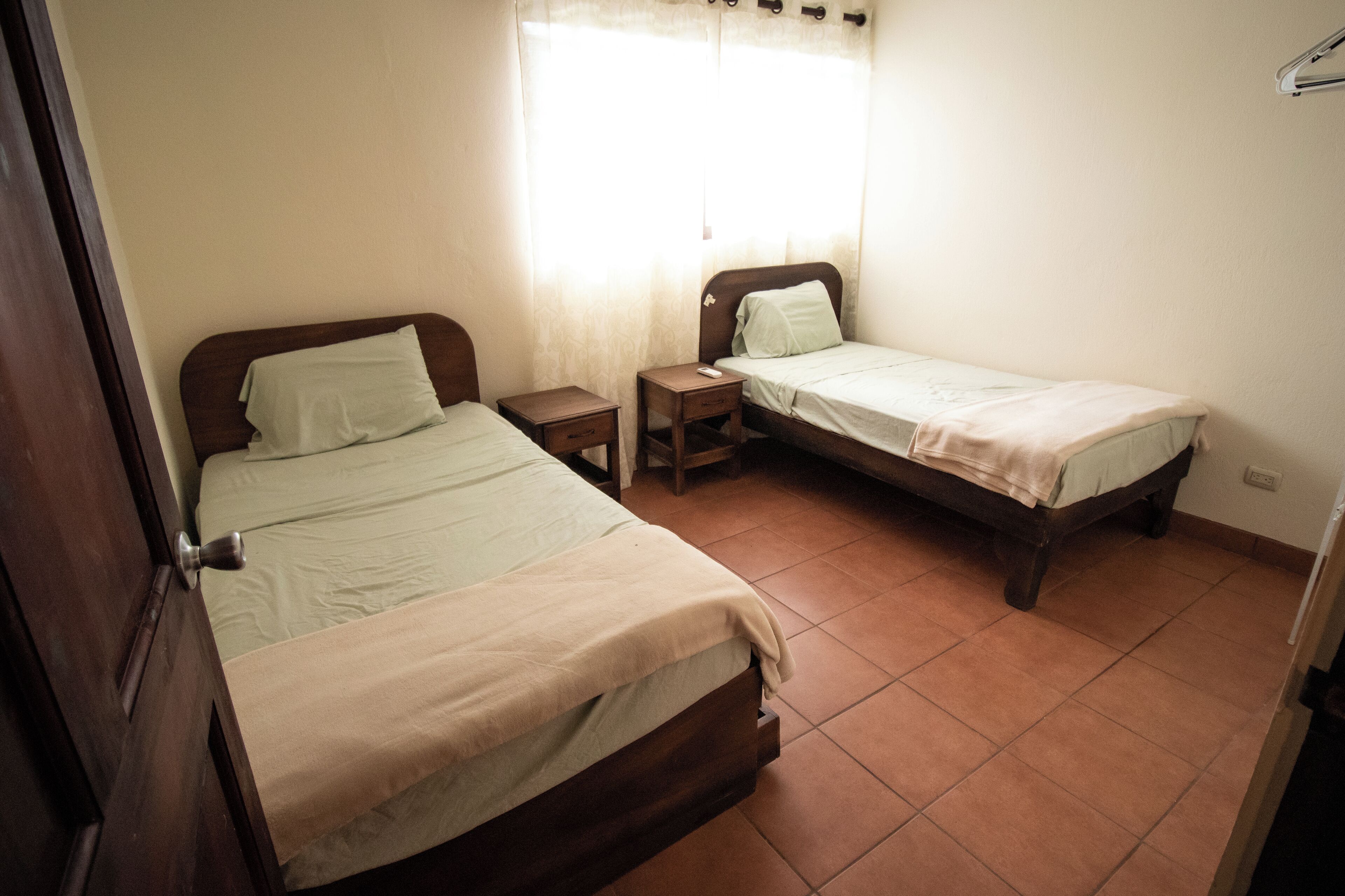 A bedroom with two single beds, a nightstand with a lamp, and a window with curtains.