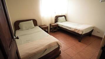 A bedroom with two single beds, a nightstand with a lamp, and a window with curtains.